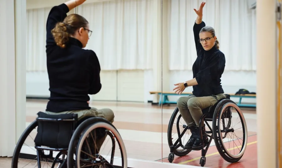 Photo de Marianne dans son studio de danse. Marianne a découvert la danse en fauteuil roulant et elle exécute des danses telles que la rumba, le paso doble et le chachacha avec son partenaire de danse. 