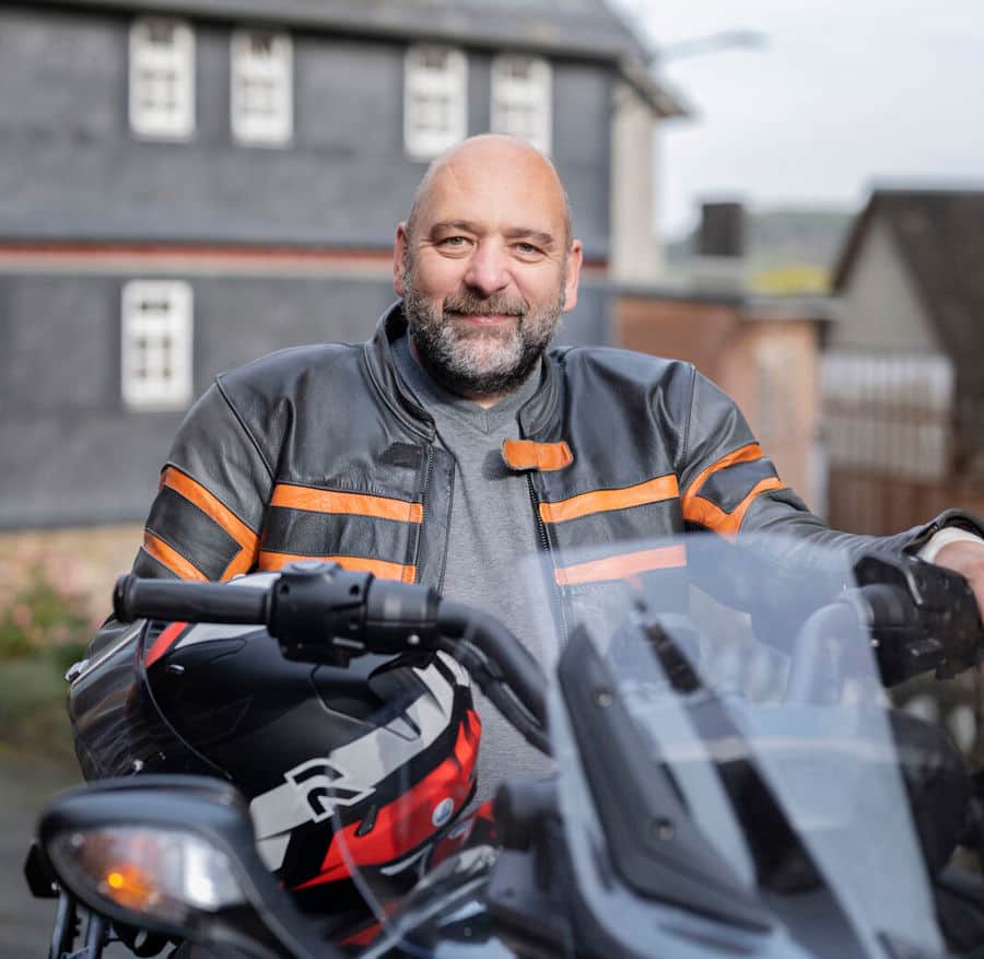 Photo portrait de Michael assis sur sa moto. Michael est atteint de sclérose en plaques et souffre de troubles urinaires. Il a découvert que sa vessie était hyperactive et qu'il devait uriner plus souvent que les autres. 